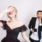 Smiling woman hiding her face playfully as a man shows a photo, symbolizing celebrity secrets behind perfect smiles